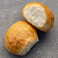 Zwei Weißbrötchen mit einer goldbraun ausgebackenen Kruste liegen auf einem grauen Untergrund. Die Kruste eines Brötchens zeigt deutlich eine Fensterung.