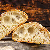 in helles und fluffiges Ciabattabrot mit sehr großen Poren in der saftigen Krume liegt vor einer dunklen Holzwand.
