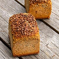 Ein in der Kastenform gebackenes Dinkelbrot mit goldbrauner Kruste und Sonnenblumenkernen auf der Oberfläche liegt auf einem verwitterten Holzuntergrund.