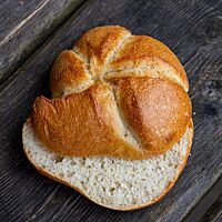 Zwei Handsemmelhälften liegen versetzt übereinander auf einem dunklen Holzuntergrund. Die luftig lockere Krume wird von einer goldbraunen, glänzenden Kruste umgeben.