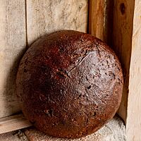 Ein runder Brotlaib mit glänzender, kräftig ausgebackener Kruste steht auf einem Mauervorsprung an eine Holzvertäfelung gelehnt.