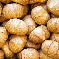 Ovale Brötchen mit goldbraun ausgebackener, glänzender, einmal quer eingeschnittener Kruste liegen übereinander auf einer Stelle.