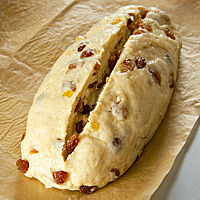 Ein eingeschnittener Stollen-Teigling liegt auf einem Backpapier.