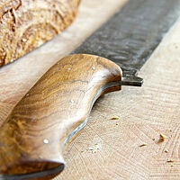 Das Damast-Brotmesser hat einen edlen, ergonomisch geformten Holzgriff.