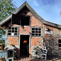 Das Backhaus in Barrigsen ist ein altes Fachwerkhaus mit rotem Klinker. Durch die geöffnete Tür kann man das Feuer im Holzbackofen bereits sehen. 