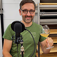 Lutz Geißler steht mit einem Glas Apfelsaft in seiner Backstube vor einem Mikrofon.