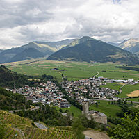 Das Örtchen Plawenn liegt in einem weiten, grünen Tal, umgeben von bewaldeten Bergen. Im Vordergrund ziehen sich Weinreben den Hanghinunter zu einer mittelalterlichen Burg.