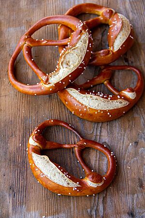 Vier an den Brezelbäuchen eingeschnittene Laugenbrezeln mit Salz auf der Kruste liegen auf einem rustikalen Holztisch.