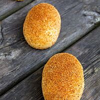 Drei goldgelb ausgebackene Bremer Kaneelbrötchen sind auf der glatten Oberfläche mit einer Mischung aus Zimt, Zucker und Semmelmehl bestreut.