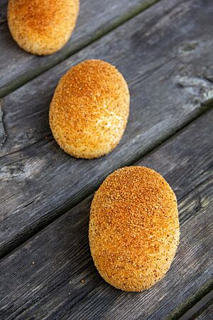 Drei goldgelb ausgebackene Bremer Kaneelbrötchen sind auf der glatten Oberfläche mit einer Mischung aus Zimt, Zucker und Semmelmehl bestreut.