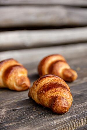 Die goldbraun ausgebackenen Butter-Croissants liegen auf einem rustikalen Holztisch.