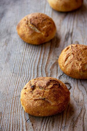 Butter-Salz-Brötchen. Kräftig ausgebackene Brötchen mit Butter und Salz auf der goldbraunen Kruste liegen auf einem Holztisch.