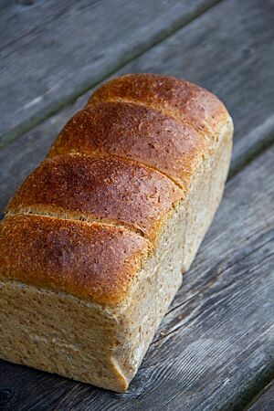 Ein eckiges Kastenbrot mit hellen Seiten und glatter dunkelbrauner Kruste oben liegt auf einem dunkelgrauen Holztisch.