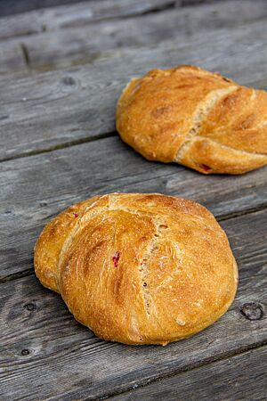 Chili-Fladen. Zwei flache goldgelbe Fladen mit flachem Ausbund liegen auf einem rustikalen Holztisch.