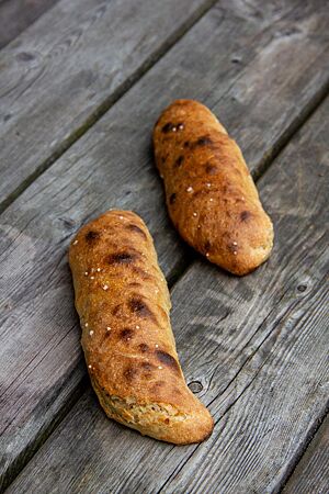 Dinkel-Einkorn-Seelen. Kräftig ausgebackene, stangenförmige Seelen liegen mit kleinen Brandspuren und weißen Salzkristallen auf der glatten Kruste auf einem grauen Holztisch.