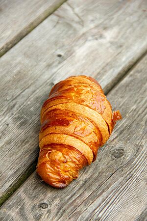 Ein goldbraun ausgebackenes Croissant mit glänzender, blättriger Kruste liegt auf einem grauen Holztisch.