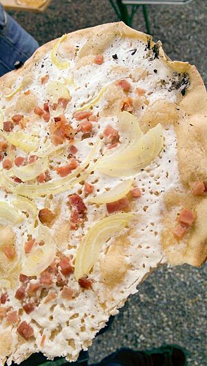 Der Flammkuchen wurde mit groben Zwiebelstücken und feinen Speckwürfeln belegt.