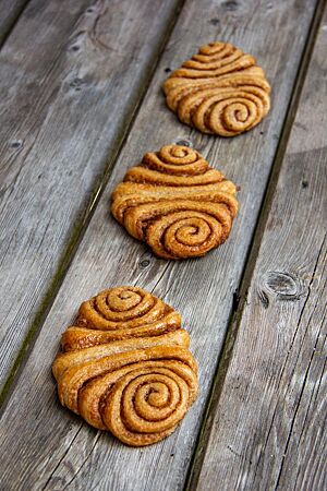 Dinkelvollkorn-Franzbrötchen. Drei flache Franzbrötchen aus Vollkornteig mit einer Zimtzucker-Füllung liegen auf einem grauen Holztisch.
