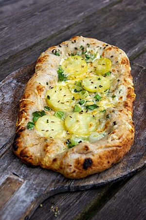 Dinnete. Die Dinnete ähnelt einer Pizza, hat jedoch eine ovale Form und ist mit Schmand bestrichen und mit Kartoffelscheiben, Lauchzwiebeln und Bergkäse belegt.