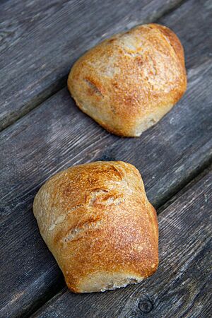 Zwei eckige Brötchen mit glatter, hellbrauner Kruste liegen auf einem dunkelgrauen Holztisch.