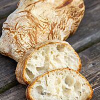 Im Anschnitt zeigt sich die grobporige, helle Krume unter der goldgelb ausgebackenen Kruste des Ciabattas.
