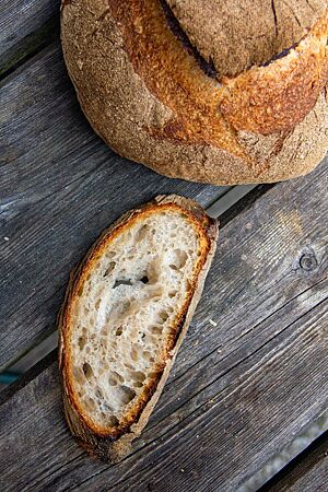 Französisches Landbrot (als Boule): offene Porung, toller Geschmack – auch dank der dunklen Kruste. Im Anschnitt zeigt sich die helle, grobporige Krume und die sehr dunkel ausgebackene, dicke Kruste.