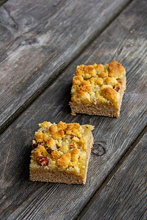 Fünfzehnprozent-Kuchen. Zwei Stücke eines Blechkuchens aus Vollkorn-Hefeteig mit Apfel- und Streuselbelag liegen auf einem grauen Holztisch.