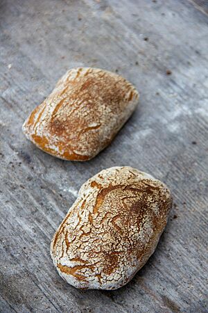 Zwei rechteckige Brötchen mit bemehlter, braun ausgebackener Kruste liegen auf einem grauen Holztisch.