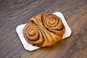 Ein goldbraun ausgebackenes Franzbrötchen mit einer Füllung aus Butter und Zimtzucker liegt auf einem Tisch.