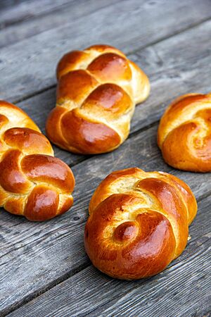 Hefezopf aus Dinkelmehl. Goldbraun ausgebackene Hefezöpfe mit glänzender Kruste liegen auf einem rustikalen Holztisch.