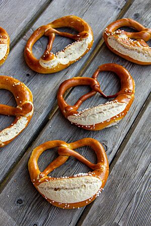 Hüttenbrezeln. Glänzende, goldbraun ausgebackene Laugenbrezeln mit aufgerissenem Bauch liegen auf einem rustikalen Holztisch.