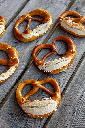 Glänzende, goldbraun ausgebackene Laugenbrezeln mit aufgerissenem Bauch liegen auf einem rustikalen Holztisch.