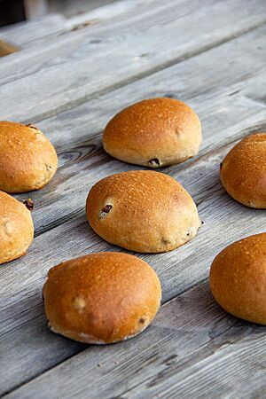 Mehrere Milchbrötchen mit einigen sichtbaren Rosinen auf der glatten Kruste liegen auf einem rustikalen Holztisch.