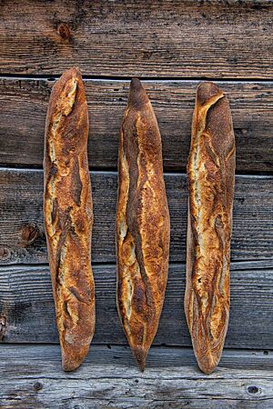 Drei kräftig ausgebackene und rustikal aufgerissene Baguettes lehnen an einer rustikalen Holzwand.