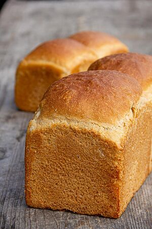 Kastenweißbrot. Das ausgebackene Kastenweißbrot mit glatter, unbemehlter Oberfläche liegt auf einem rustikalen Holztisch.
