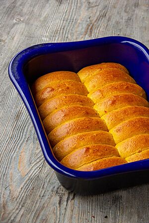 Sechzehn längliche Kürbisbrötchen liegen eng aneinandergereiht und goldgelb ausgebacken in einer Auflaufform.