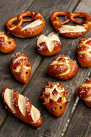 Fantasievoll geformtes Laugengebäck liegt auf einem Holztisch – als Igel, Maus, Brezel, Knoten usw.