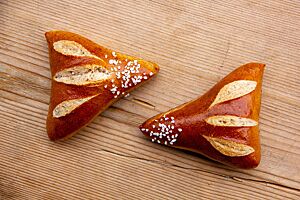 Laugengipfel. Zwei dreieckige Laugengipfel mit glänzender Kruste sind auf der Grundseite eingeschnitten und auf der Spitze mit Brezelsalz bestreut.