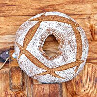 Ein ringförmig gebackenes Brot mit bemehlter Kruste steht vor einer rustikalen Holzwand.