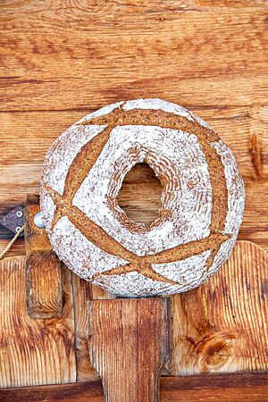 Ein ringförmig gebackenes Brot mit bemehlter Kruste steht vor einer rustikalen Holzwand.