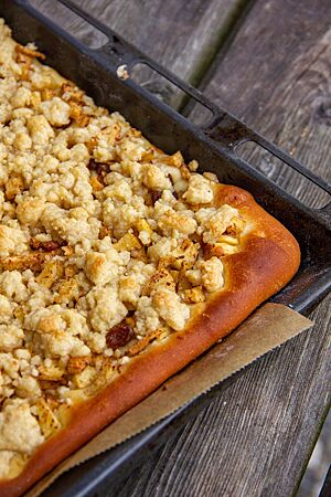 Mürbehefeteig (geschichtet). Der geschichtete Mürbehefeteig liegt goldbraun ausgebacken als Apfel-Streusel-Kuchen auf einem Backblech.