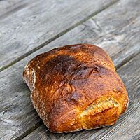 Ein quadratisch abgestochenes und kräftig ausgebackenes Brot mit glatter Kruste liegt auf einem rustikalen Holztisch.
