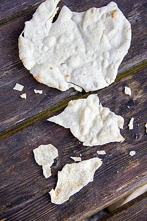 Pane Carasau. Das hauchdünne, knusprig ausgebackene Fladenbrot liegt auf einem rustikalen Holztisch.