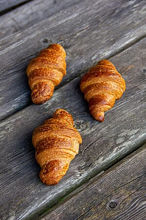 Drei goldbraun ausgebackene Croissants mit glänzender Oberfläche liegen auf einem rustikalen Holztisch.