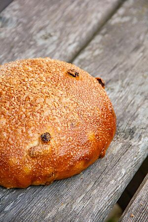 Ein goldbraun ausgebackenes, rundes Brot liegt auf einem rustikalen Holztisch.