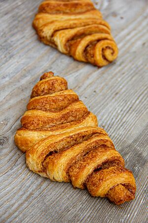 Auf einem rustikalen Holztisch liegen zwei goldbraun ausgebackene, saftige Franzbrötchen.