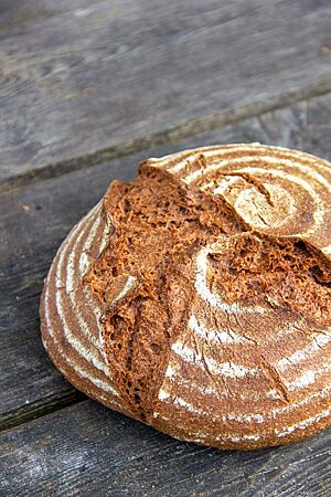 Reinkornbrot (Vollkornbrot mit Einkorn und Rotkornweizen). Das kräftig ausgebackene Reinkornbrot mit rustikal aufgerissener und leicht bemehlter Kruste liegt auf einem Holztisch.