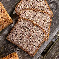 Drei Scheiben desBuchweizen-Kastanien-Erdmandel-Brotes zeigen die saatenreiche Krume umhüllt von einer goldbraun ausgebackenen Kruste.
