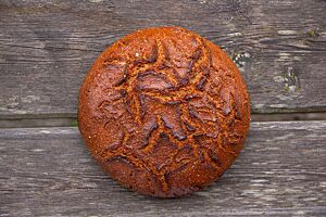 Das kräftig ausgebackene Roggenbrot mit leicht glänzender Oberfläche liegt auf einem rustikalen Holztisch.