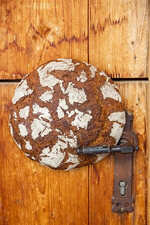 Ein runder Roggenbrot-Laib klemmt zwischen Türblatt und Klinke einer Holztür.